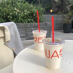 two cups with red straws sitting on top of a white table next to each other