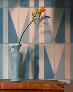 a single flower in a blue vase on a wooden table next to a tiled wall