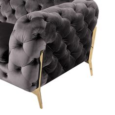 a grey velvet chair with gold legs and buttons on the armrests, viewed from the front