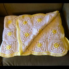 a crocheted blanket sitting on top of a couch next to a pillow with yellow flowers