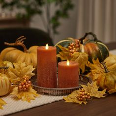 two candles on a table surrounded by autumn leaves