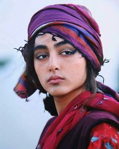 a young man wearing a purple and red headdress is looking at the camera