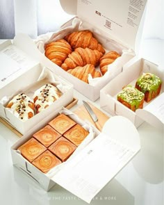 four different types of pastries in white boxes on a table with papers and scissors