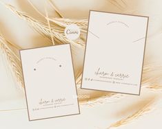 two white cards with gold foil on them sitting next to some wheat stalks and leaves