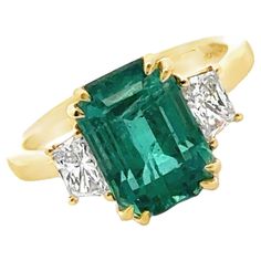 This Emerald & Diamond Cocktail Ring showcases a stunning 4.00-carat emerald-cut Zambian emerald, certified by GIA for its exceptional quality (F2 grade). Flanking the vibrant green emerald are two elegant trapezoid diamonds, totaling 0.70 carats (G color, VS clarity), adding brilliance and symmetry to the design. In a classic 18 karat yellow gold setting, this size 6.25 ring exudes timeless sophistication (can be sized), and measures 10 x 15mm on top. Princess Cut Emerald Ring, Emerald And Ruby Ring, Star Sapphire Gemstone, Art Deco Sapphire Ring, Oval Sapphire Ring, Yellow Gold Cocktail Ring, Sapphire Eternity Ring, Orange Ring, Art Nouveau Ring