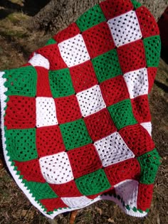 a crocheted blanket sitting on the ground next to a red and white object