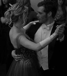 a man and woman are dancing together at a formal event with people in the background