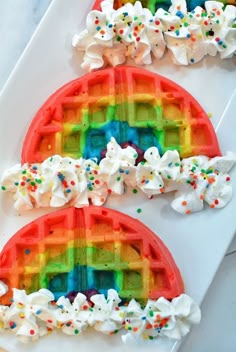 two rainbow waffles with white frosting and sprinkles on them