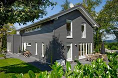 a gray house sitting on top of a lush green field next to trees and bushes