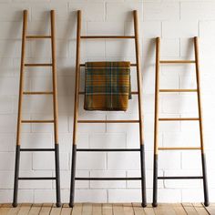 three wooden ladders against a white brick wall with a plaid towel hanging on it