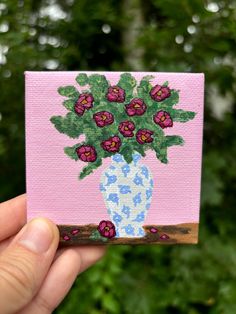 a hand holding up a small card with a painting of flowers in a vase on it