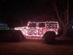 a jeep covered in christmas lights parked next to a tree