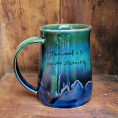 a blue and green coffee mug sitting on top of a wooden table with the words seaweed over storm written below it