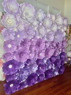 purple and white paper flowers are arranged on the wall