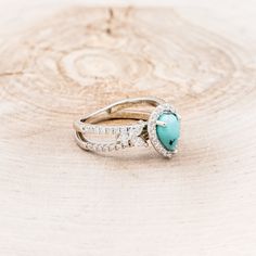 a turquoise heart shaped ring on top of a piece of wood with diamonds around it