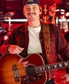 a man holding a guitar in his right hand and wearing a hat on top of his head