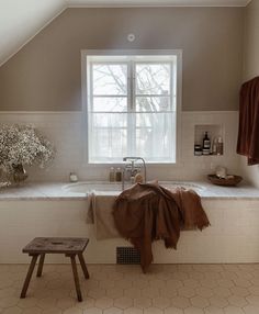 a bath room with a large tub and a wooden bench in front of a window