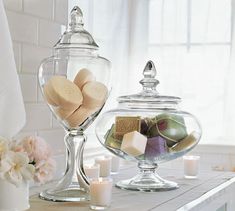 two glass jars filled with soaps and candles on a table next to some flowers