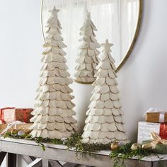 three white christmas trees sitting on top of a wooden table next to presents and a mirror