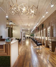 the inside of a hair salon with lots of chairs and lights hanging from the ceiling