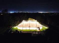 a large tent is lit up at night with lights on the grass and trees around it