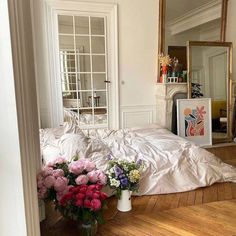 a bed with white sheets and flowers on the floor in front of a large mirror