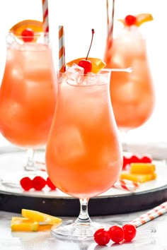 three glasses filled with drinks and garnished with pineapple, cherries, and candy canes