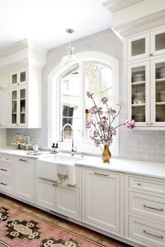 a large kitchen with white cabinets and flowers in the window sill on the counter