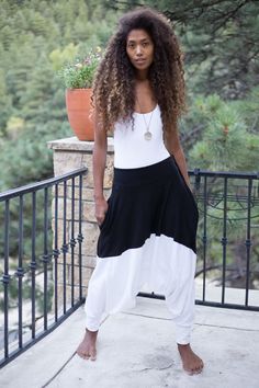 a woman standing on a balcony with her hair blowing in the wind and wearing black and white pants