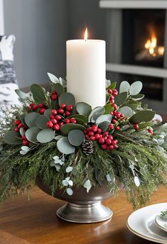 a candle sits on top of a table with greenery, berries and pine cones