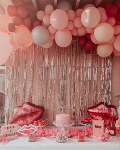 a table topped with lots of balloons and cake next to a wall covered in streamers