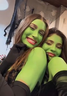 two women in green make up their faces and smile at the camera while posing for a photo