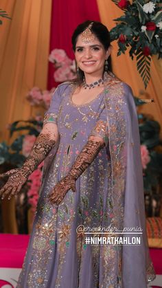 a woman in a purple dress with her hands on her chest and arms outstretched, posing for the camera