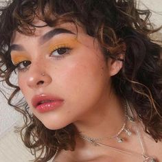 a close up of a woman with curly hair and orange eyeshadow wearing a necklace