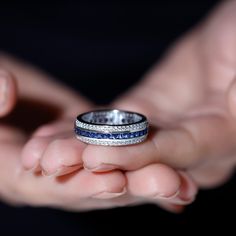 a person holding a ring in their hand with blue and white stones on the band