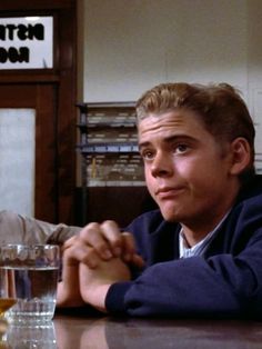 two young men sitting at a table with glasses in front of them, one looking up