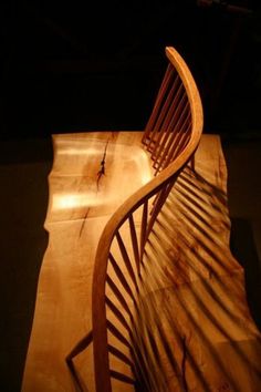 a curved wooden bench sitting in the middle of a dark room with light shining on it