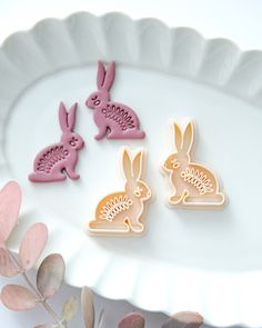 three cookies shaped like bunnies sitting on top of a white plate next to leaves