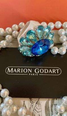 MARION GODART Paris Bague Fleur Bleu Strass taille 59 eu Spectacular statement rhinestone flower ring handmade by Marion Godart. It features a large blue faceted prong set rhinestone surrounded by 10 drop-shaped light blue rhinestones creating a mid-century style flower ring. The whole sits on a hard as glass white resin base-ring. This impressive ring measures a little over 1 3/4 inch diameter and 5/8 inch high, US ring size 9. This ring is unique, completely designed and handmade by Marion God Blue Jeweled Rings For Gift, Blue Jeweled Rings For Gifts, Blue Crystal Rings For Party, Sharon Miller, Paris Bracelet, French Jewelry, Scarf Rings, Bold Rings, French Designer