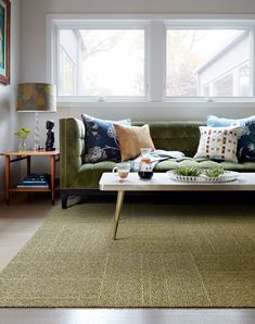 a living room with green couches and pillows on the floor next to a window