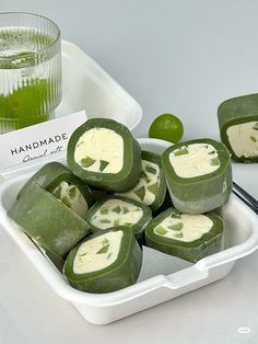 several pieces of green and white food in a container next to a glass of lime juice