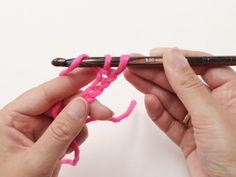 two hands crocheting the end of a piece of pink yarn