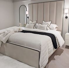 a bed with white sheets and pillows in a bedroom next to a mirror on the wall