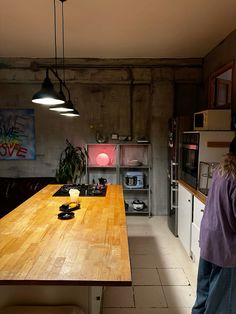 a woman standing in a kitchen next to a wooden table and stove top on a tiled floor