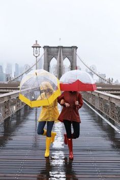 two women walking across a bridge holding umbrellas