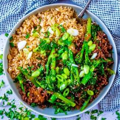 a bowl filled with rice and vegetables on top of a blue cloth next to a spoon