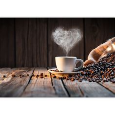 a cup of coffee with steam rising out of it and beans scattered around on a wooden table