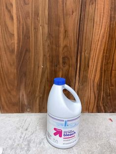 a gallon of liquid sitting on the ground next to a wood paneled wall,