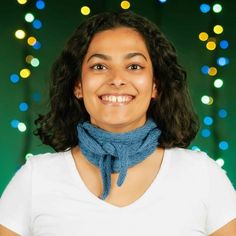 a woman wearing a blue scarf and smiling at the camera with christmas lights in the background