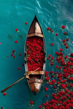 a boat filled with lots of red flowers floating on top of blue water next to shore